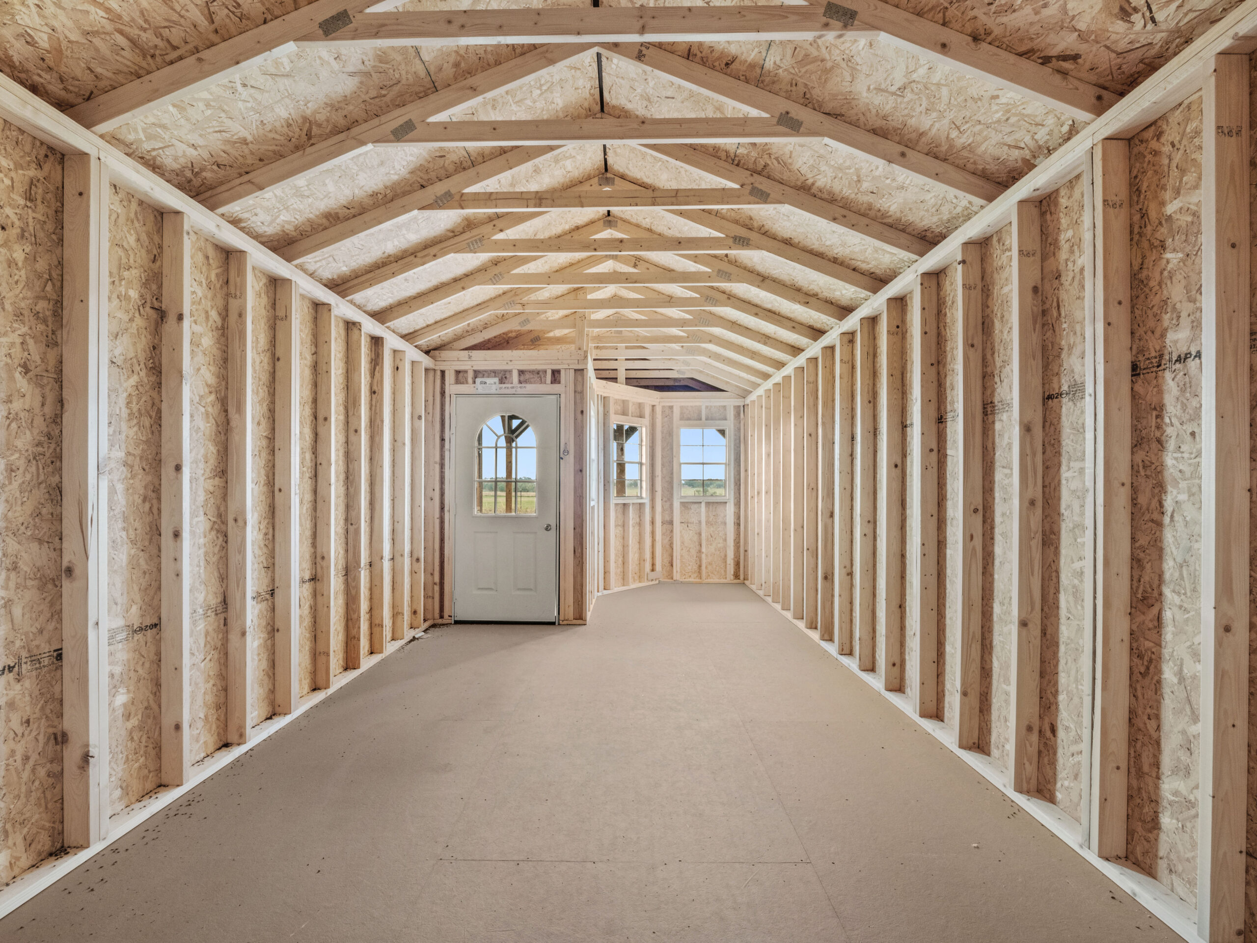 Long unfinished cabin shed interior featuring open wood rafter ceiling trusses, stud wall framing, smooth floor, and a entry door in Chattanooga, Tennessee.