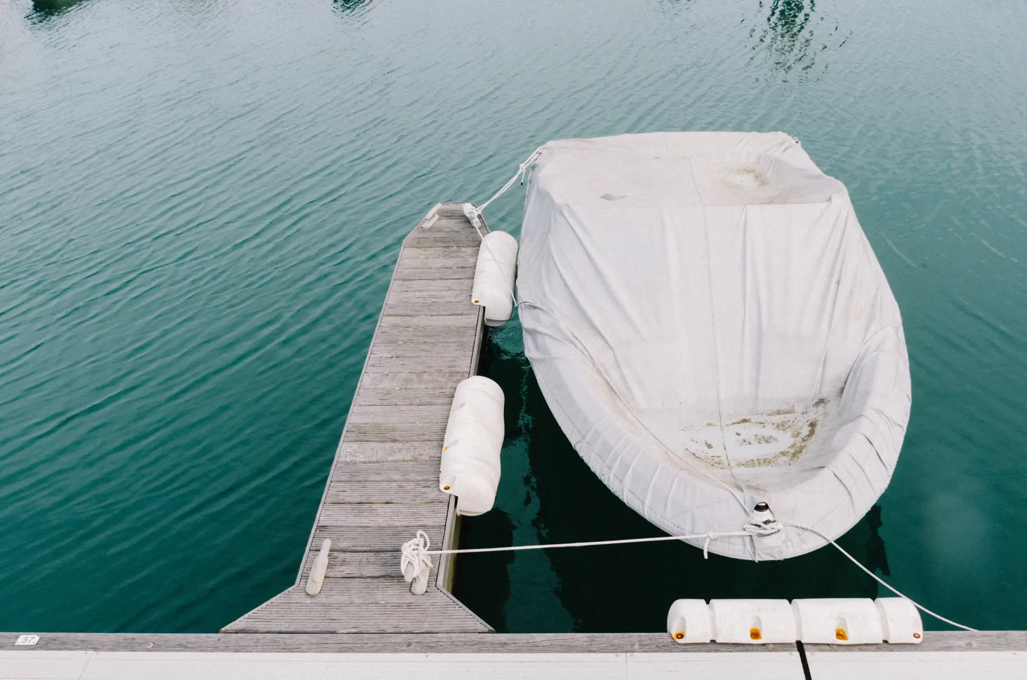 Small boat secured to a wooden dock floating in clear green water and fully protected by a custom fitted white marine canvas cover in Venice, FL.