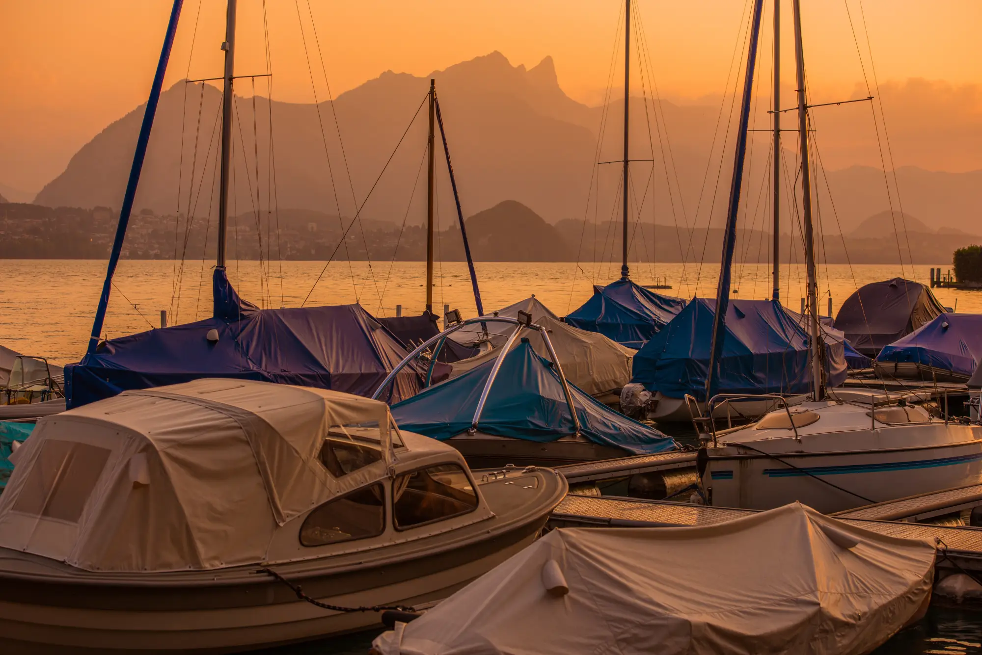 Docked sailboats and powerboats with custom protective canvas covers and bimini tops at a marina during sunset in Sarasota, FL.