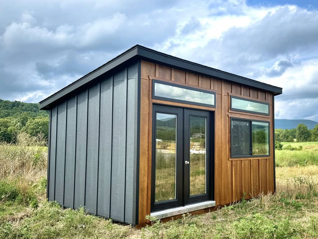 Modern studio shed featuring natural wood vertical paneling, dark grey siding, transom windows, and glass double doors set in Burlington, Vermont.