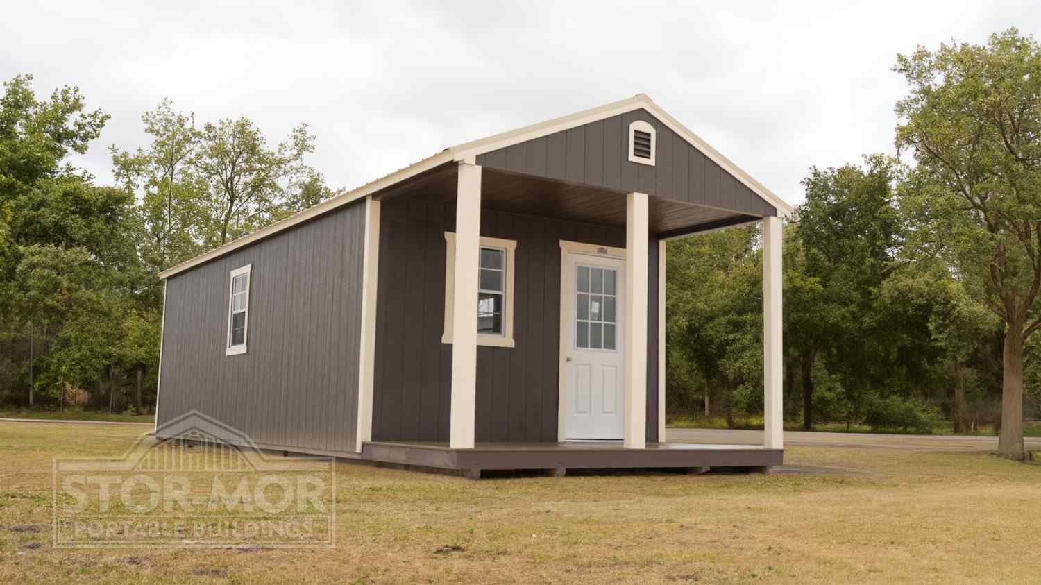Dark brown cabin shed with cream trim featuring a spacious covered front porch with support posts and a white entry door in Chattanooga, Tennessee.