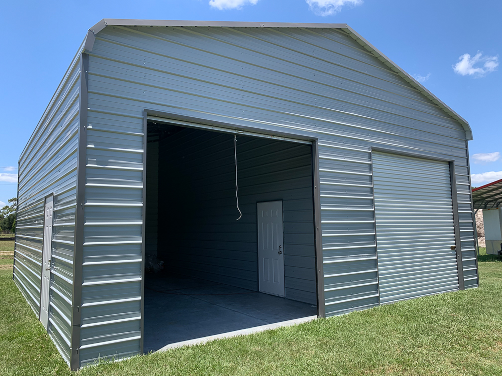 Large light blue metal workshop with dark grey trim, featuring one open high-clearance roll-up garage door Bay and one closed roll-up door on a grassy lawn in Gainesville, FL.