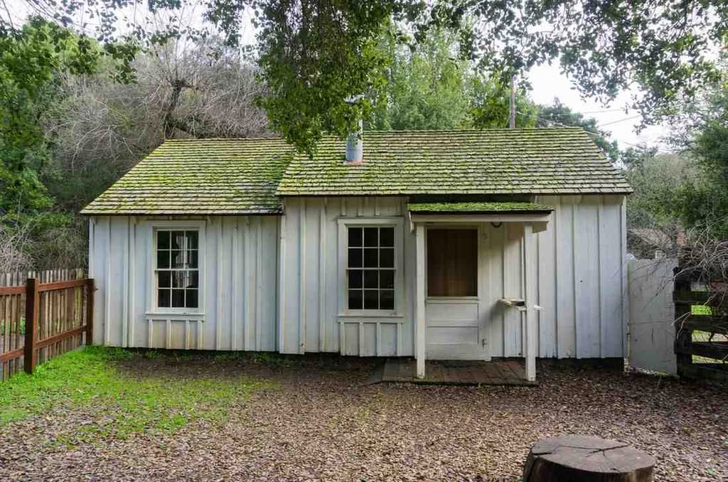 A rustic white board-and-batten cabin shed featuring a small front entry porch, multi-pane windows, and a green shingle roof in Dallas, TX.
