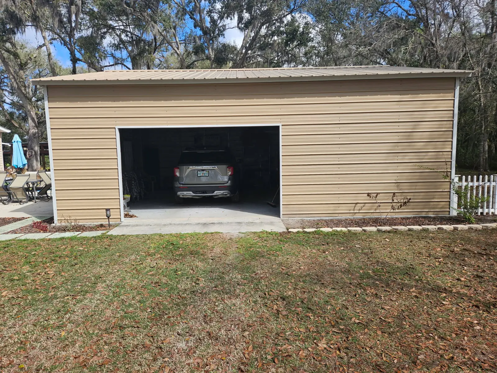 A tan metal garage building with an open main door showing an SUV parked inside on a concrete pad in Dallas, TX.