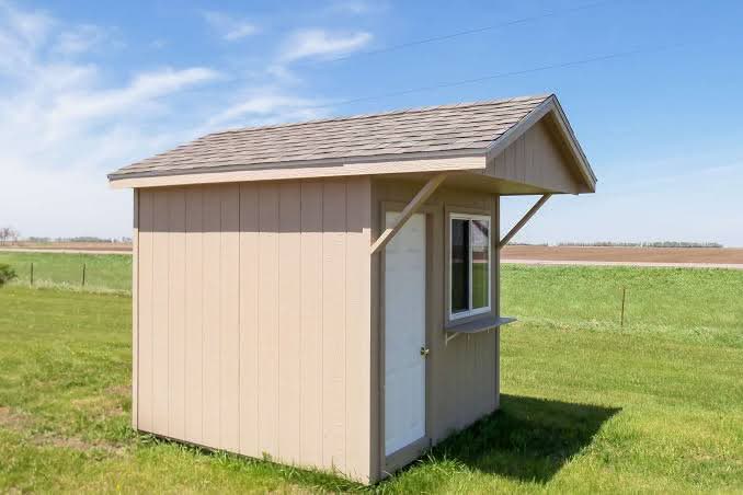 Tan wooden concession shed with an extended roof overhang, serving window with counter ledge, and side entry door in Des Moines, Iowa.