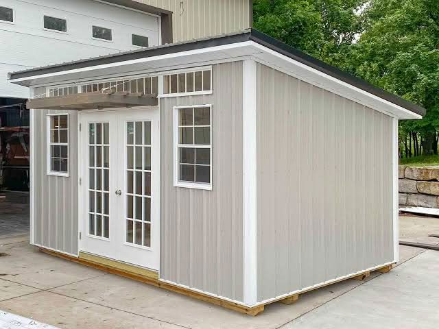 A light gray modern lean-to studio shed featuring white-framed double french doors, transom windows, and a small porch awning in Dallas, TX.