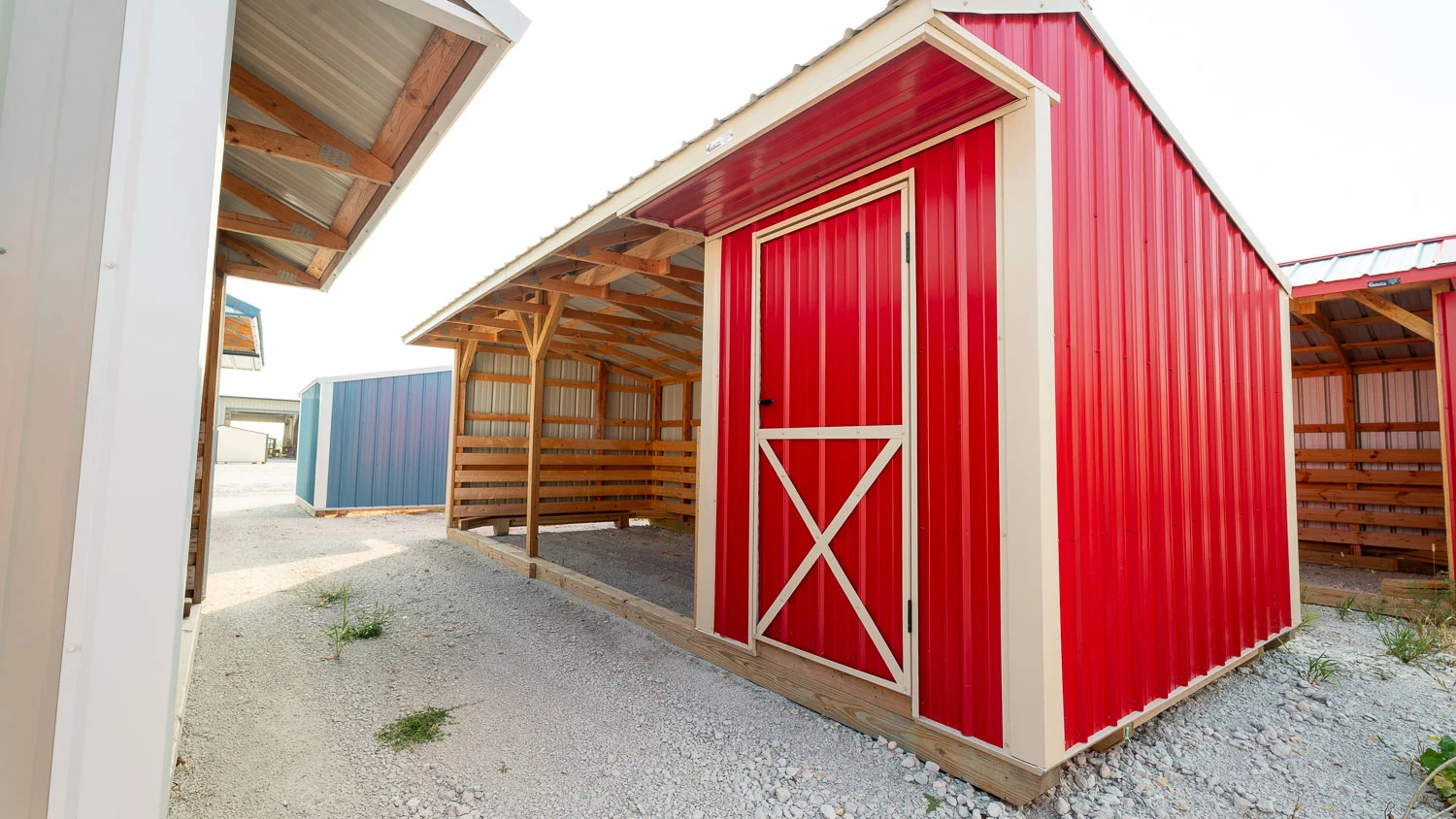 Bright red metal run-in livestock shelter featuring beige trim, an open-front loafing bay with wood kickboards, and an attached side tack room with a door in Ocala, Florida.