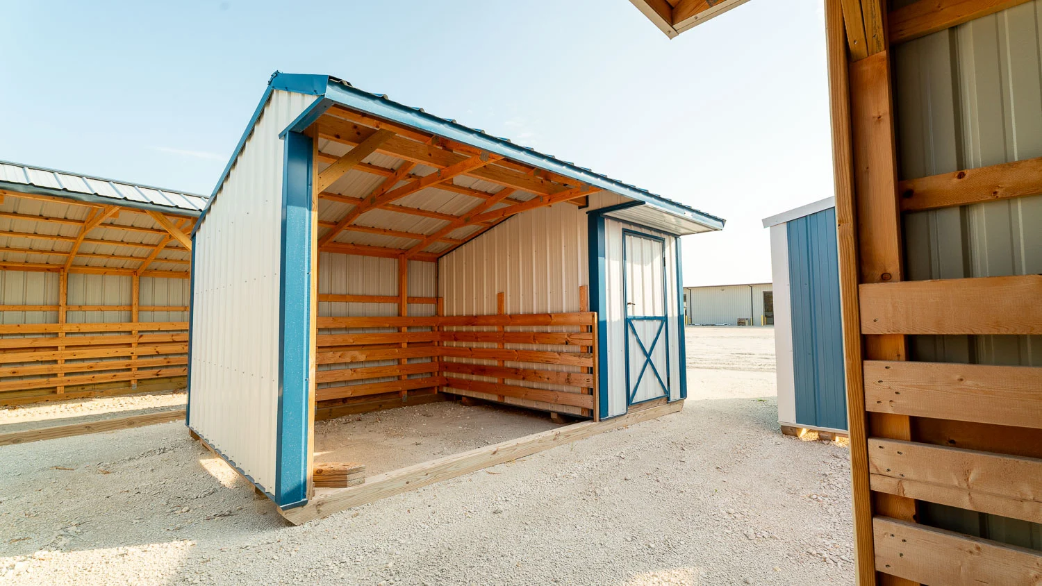 Blue and white metal run-in livestock shed featuring an open loafing bay with kickboards and an attached lockable tack room with a door in Lexington, Kentucky.