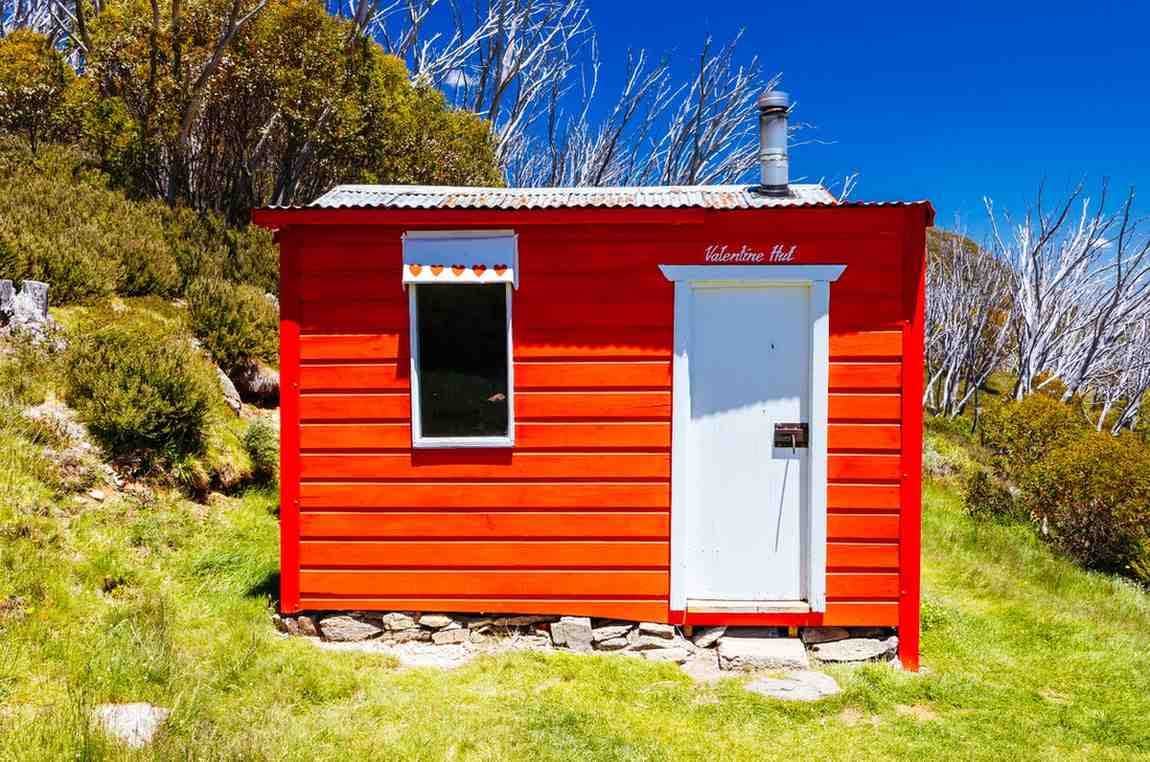 Bright red mountain cabin rental named Valentine Hut nestled on a grassy hill with blue skies in Asheville, North Carolina.
