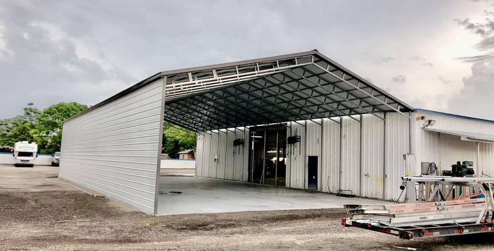Large commercial metal carport shelter with a high-clearance roof and open front attached to an industrial steel building on a paved lot in Commercial Point, FL.