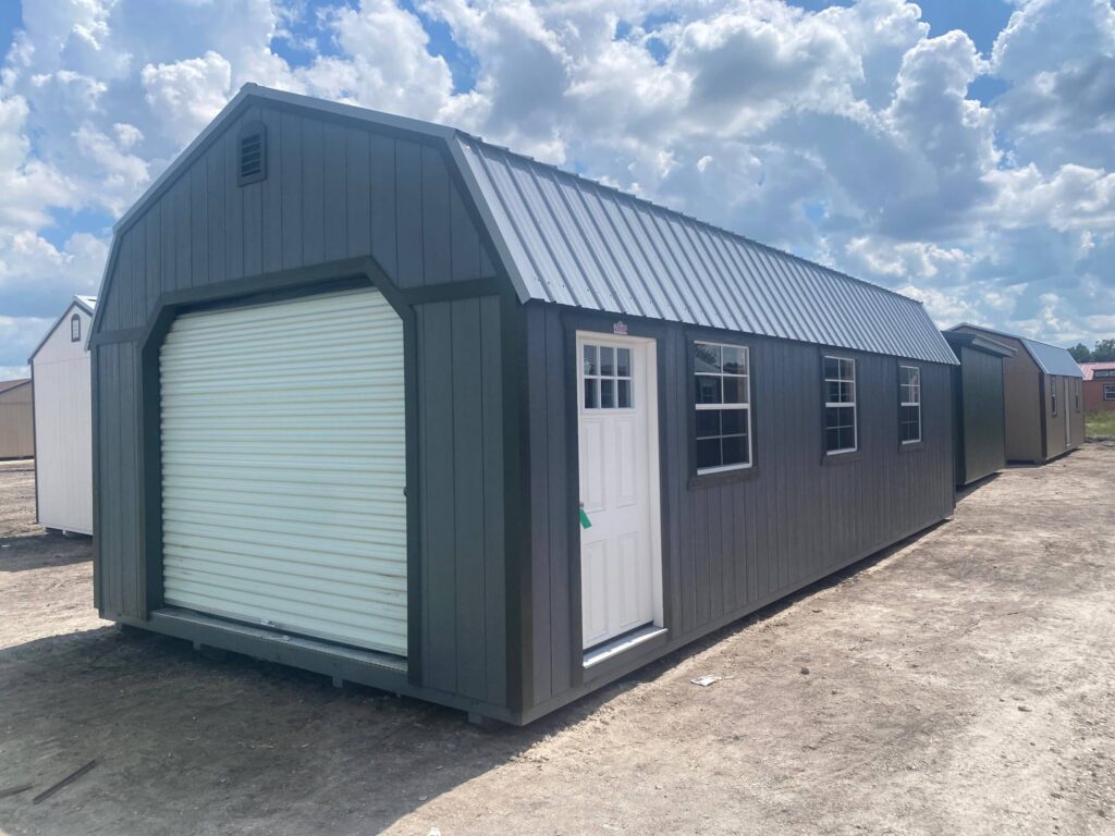 Exterior view of a charcoal grey high-barn garage shed featuring a white front roll-up door, side house door, windows, and silver metal roof in Chiefland, FL.