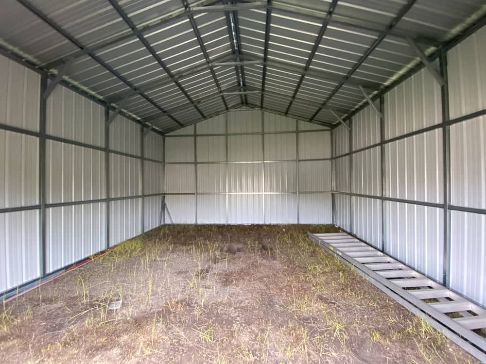 Red custom metal barn building with white trim, open lean-to side bays, main drive-through opening, framed windows, and steel framing on an asphalt lot in Brooksville, FL.