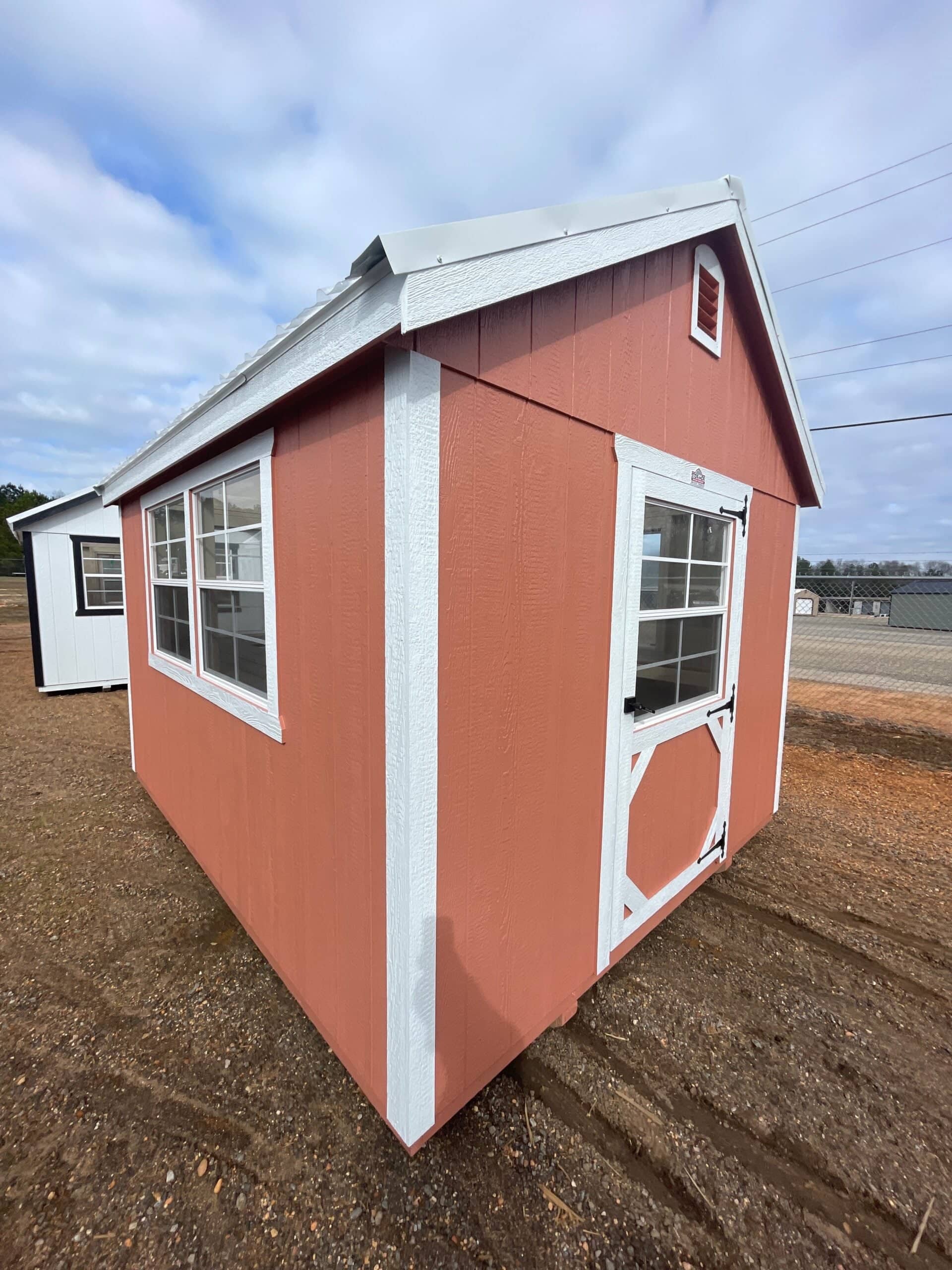 Terracotta red custom wooden garden shed with bright white trim, a metal roof, side grid windows, and an end door with a glass pane in Inverness, FL.