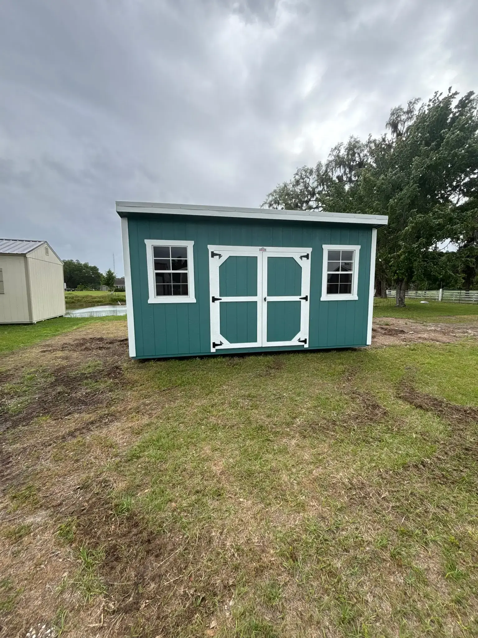 Teal green custom wooden shed with white trim, double center doors, two side windows, and a modern lean-to roof sitting on a grassy yard in Gainesville, FL.