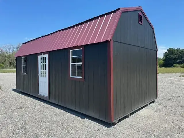 Dark charcoal grey wooden lofted barn cabin shed featuring dark red metal gambrel roof, red trim, white glass door, and grid windows in Inverness, FL.