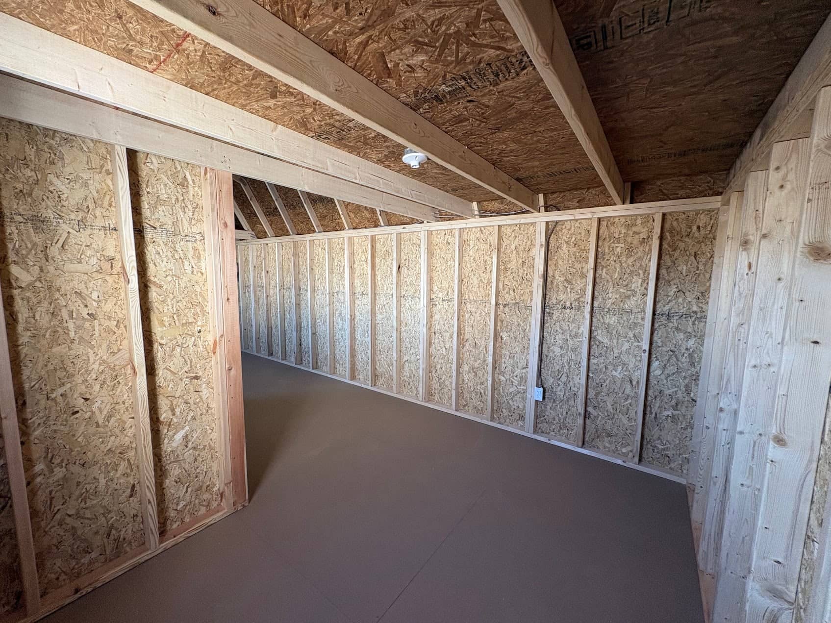 Unfinished wooden shed interior showing OSB wall panels, natural wood studs, built-in overhead storage loft framing, and clean flooring in Chiefland, FL.