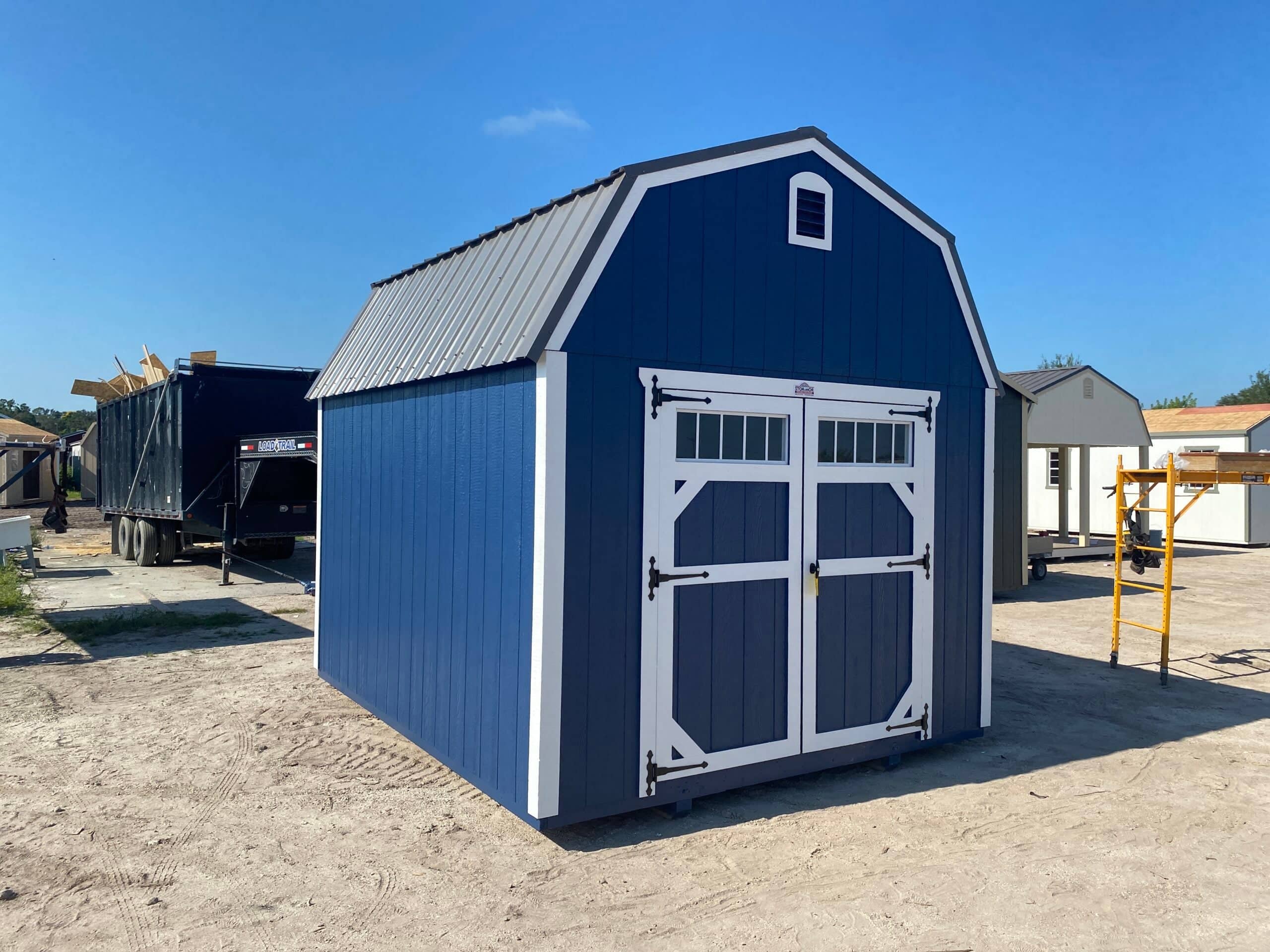 Navy blue lofted barn storage shed featuring crisp white trim, a silver metal gambrel roof, and double front doors with transom windows in Brooksville, FL.