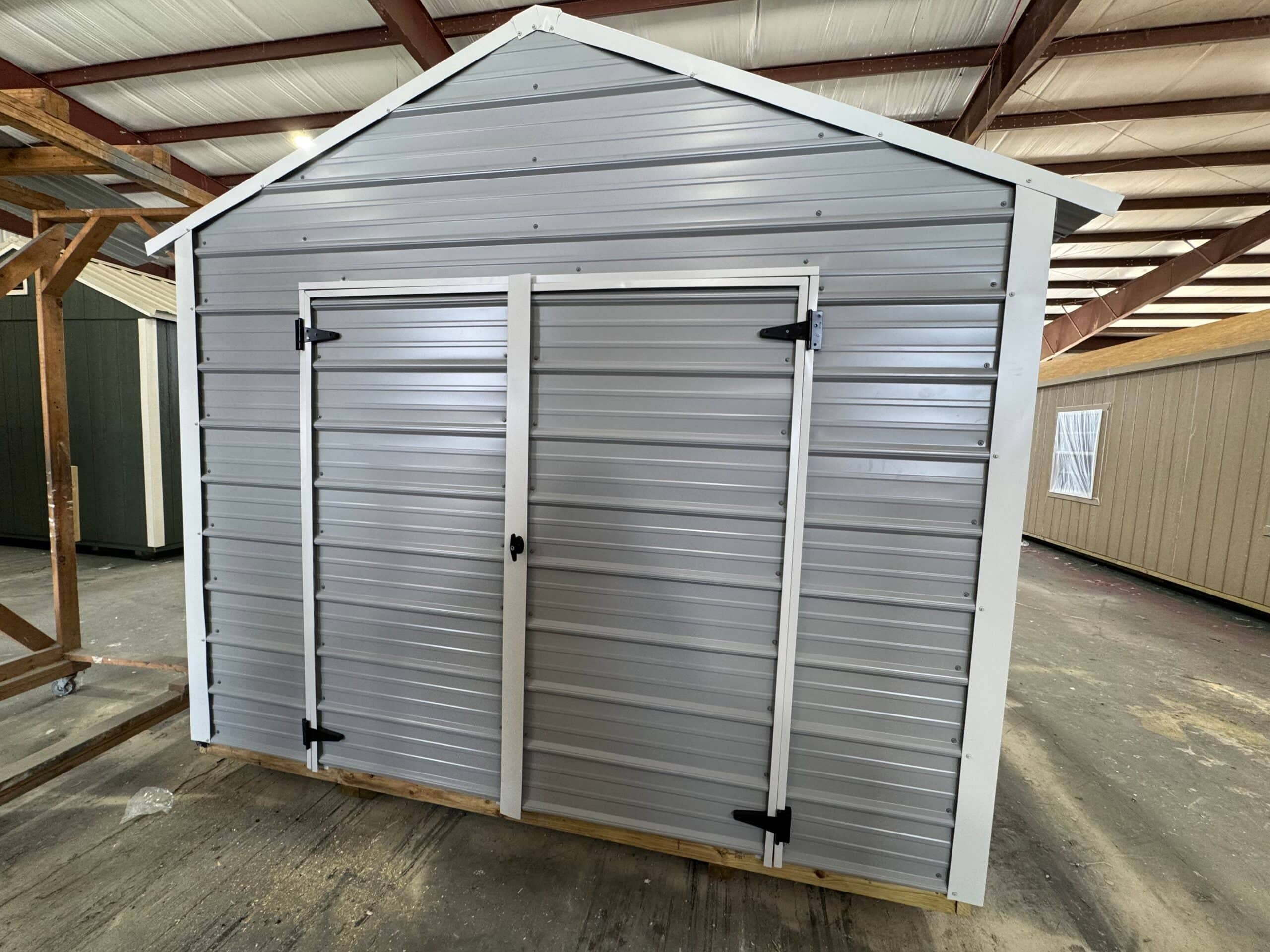 Light grey metal storage shed with horizontal steel siding, white trim, and double door entry inside a display warehouse in Alachua, FL.