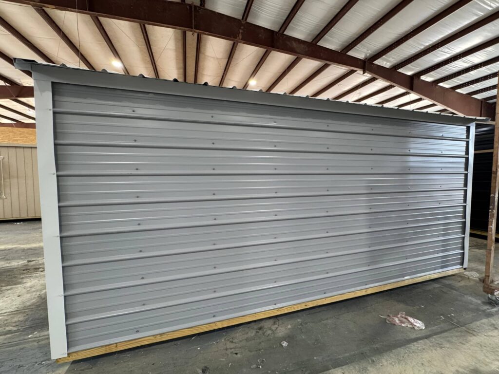 Exterior side view of a durable grey metal storage building with white trim resting on a treated wooden base inside a warehouse in Crystal River, FL.
