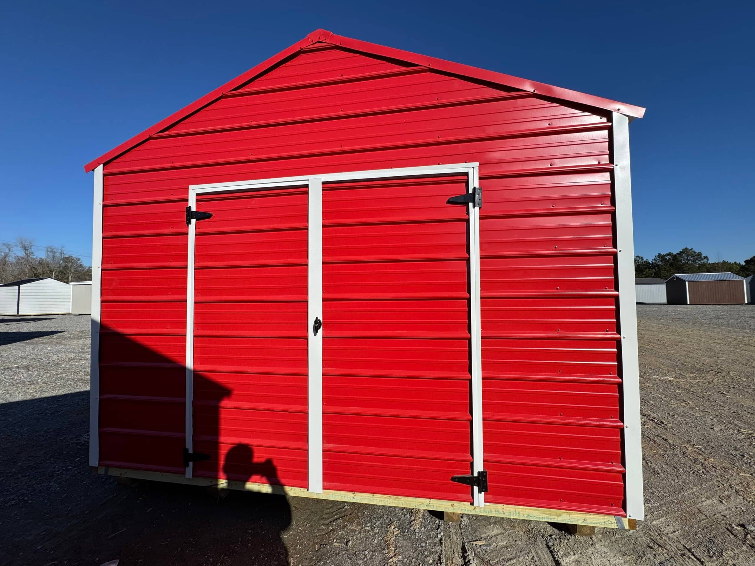 Bright red metal storage shed with white trim and large double doors sitting on a gravel lot in Brantley County, FL.