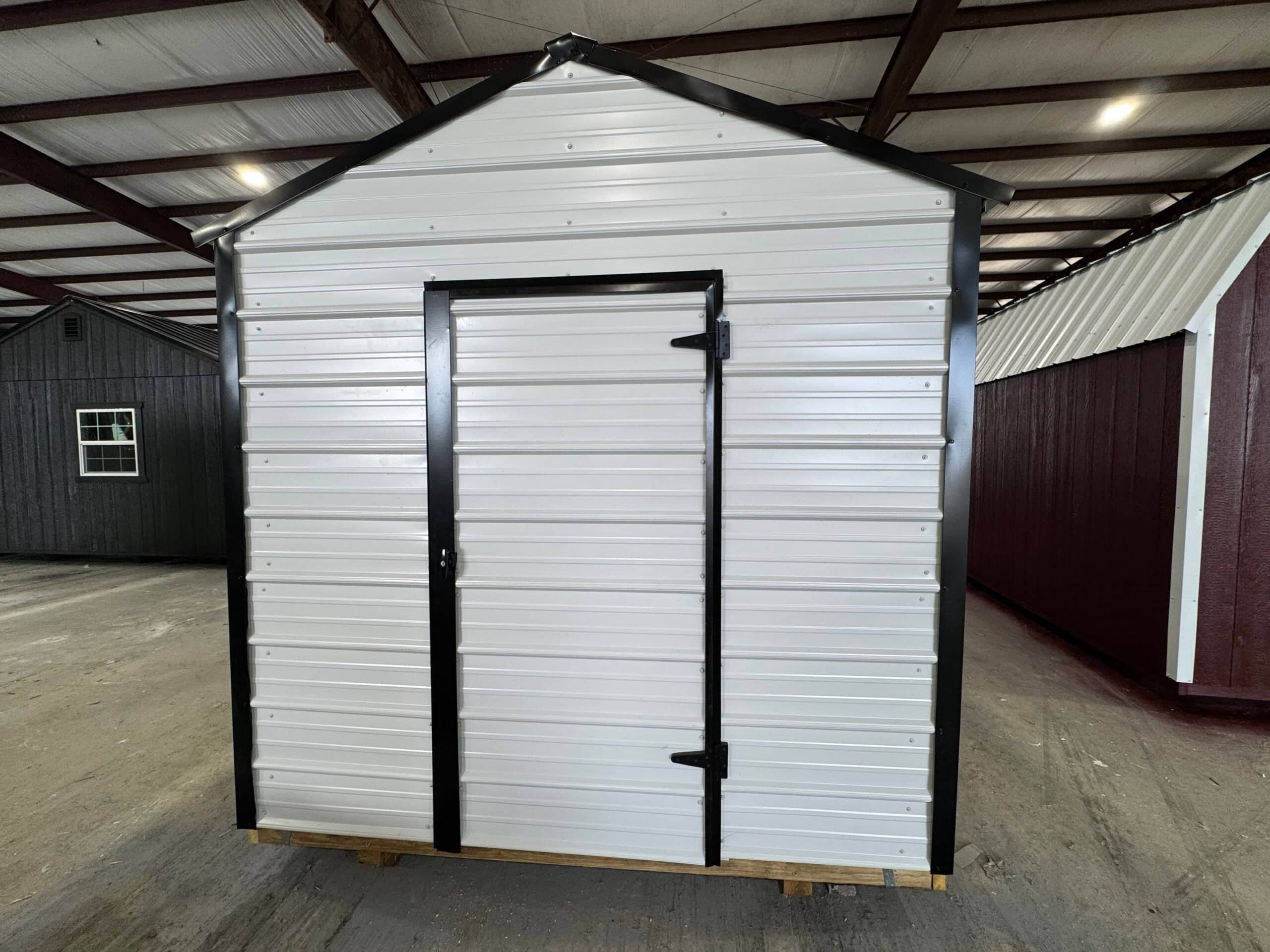 Front view of a white metal utility storage shed with black trim and a single entry door inside a indoor display showroom in Dunnellon, FL.
