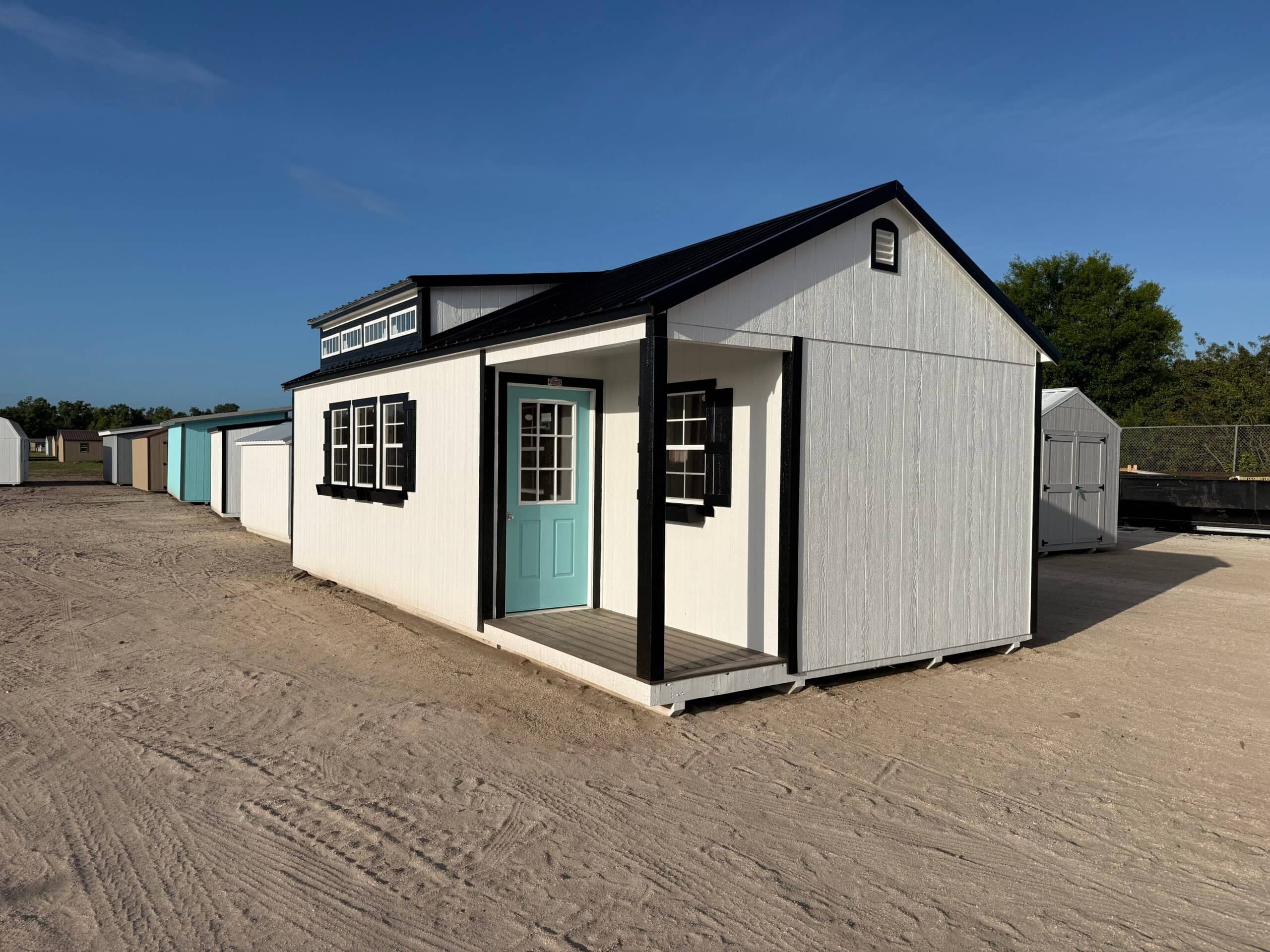 Exterior view of modern accessory buildings featuring white siding, black trim accents, a vibrant turquoise door, small porch, and dormer windows in Dunnellon, FL.