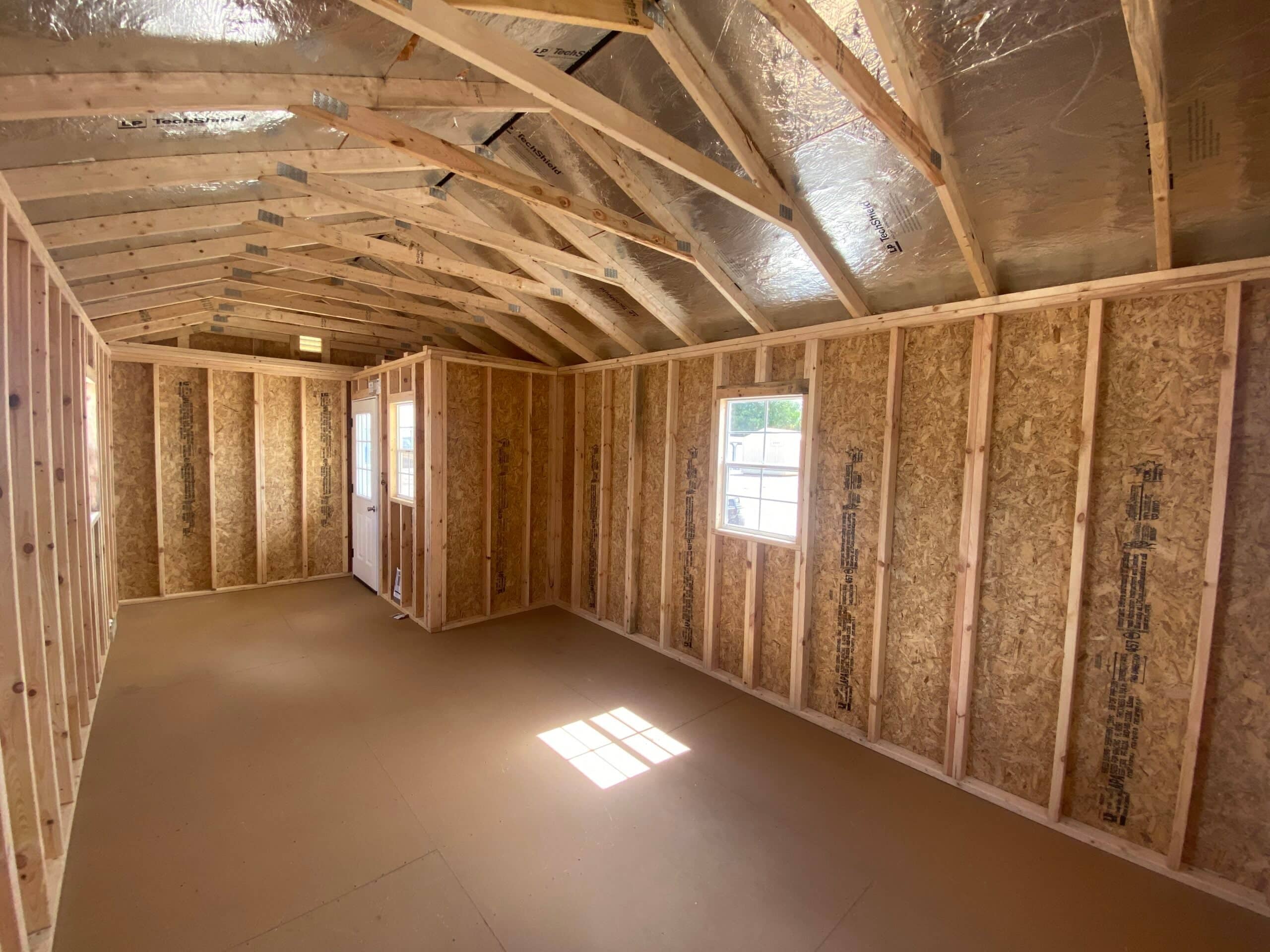 Interior view of unfinished custom wooden shed framed with radiant barrier roof decking, OSB wall panels, wooden roof trusses, and a side window in Chiefland, FL.