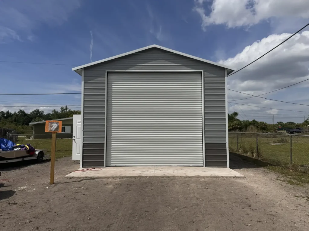 Newly built tall grey two-tone RV metal garage with a large white roll-up door and side walk-in door on a concrete pad in Lakeland, FL.