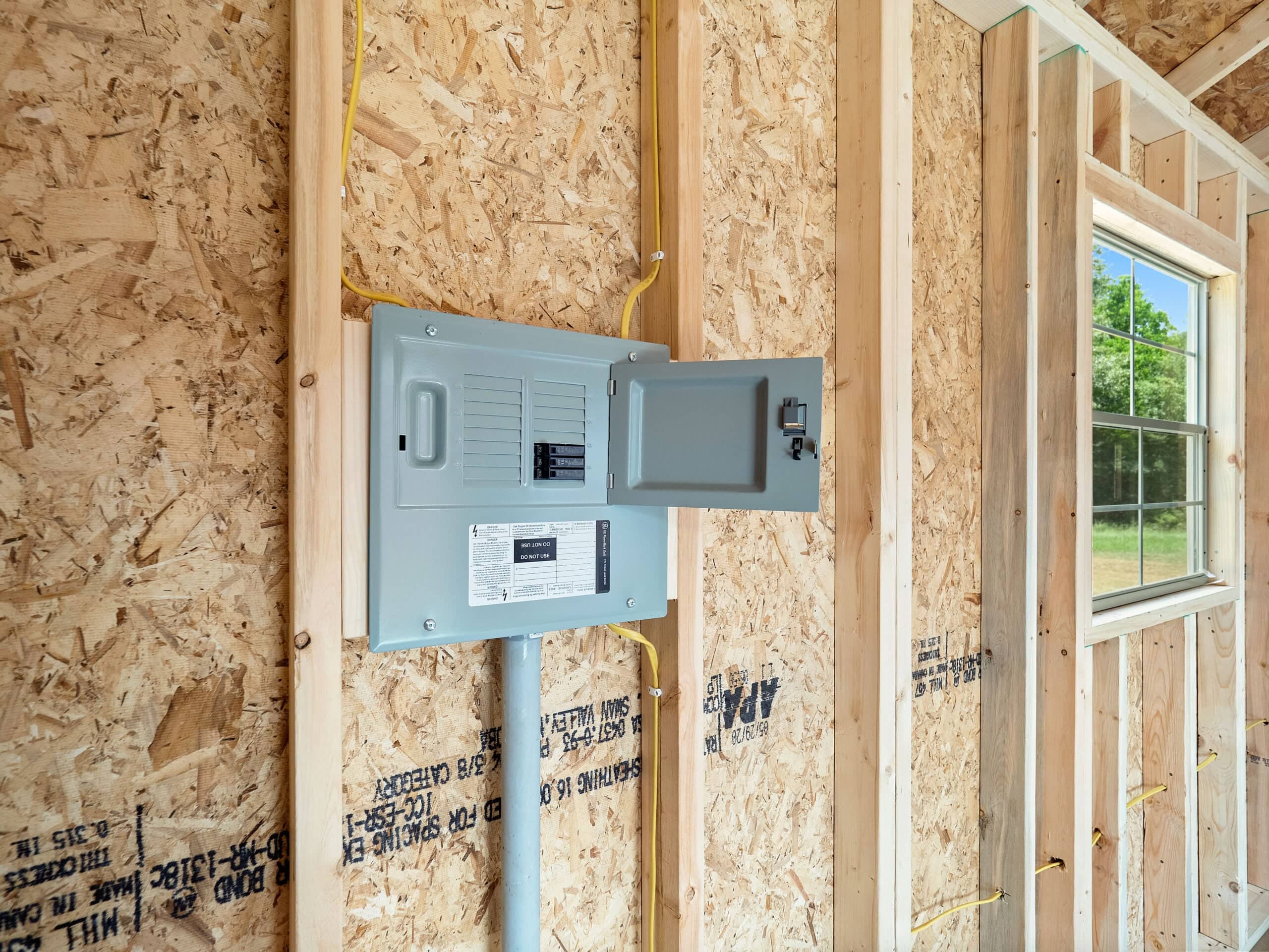 Open grey electrical breaker panel installed on wooden wall studs with exposed yellow wiring inside an unfinished shed in Gainesville, FL.
