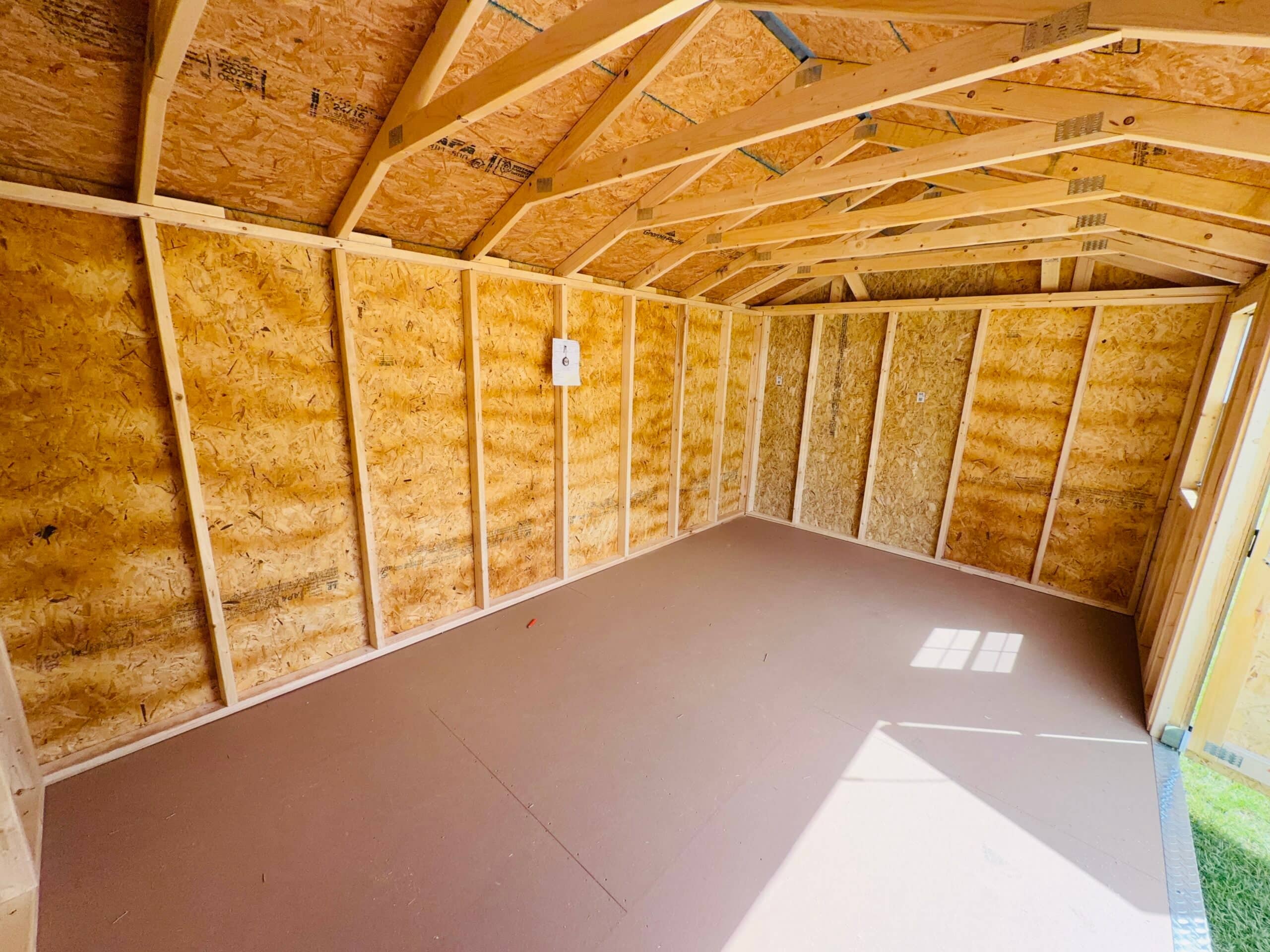 Interior view of an unfinished wooden utility storage shed featuring exposed stud framing, OSB wall panels, roof trusses, smooth composite flooring, and natural light casting through an open door in Gainesville, FL.