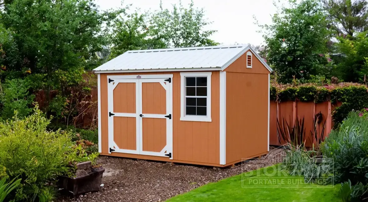 Warm orange-brown wooden side utility shed with white trim, double entry doors, side grid window, white metal roof, and upper gable vent in a backyard in Gainesville, FL.