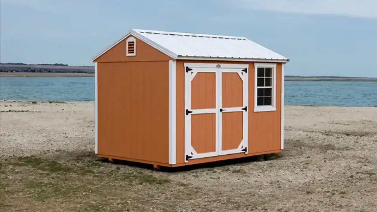 Bright orange wooden utility storage shed with white trim, a white metal roof, double doors, and a grid window set near the water in Crystal River, FL.